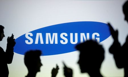 FILE PHOTO - People pose with mobile devices in front of projection of Samsung logo in this picture illustration