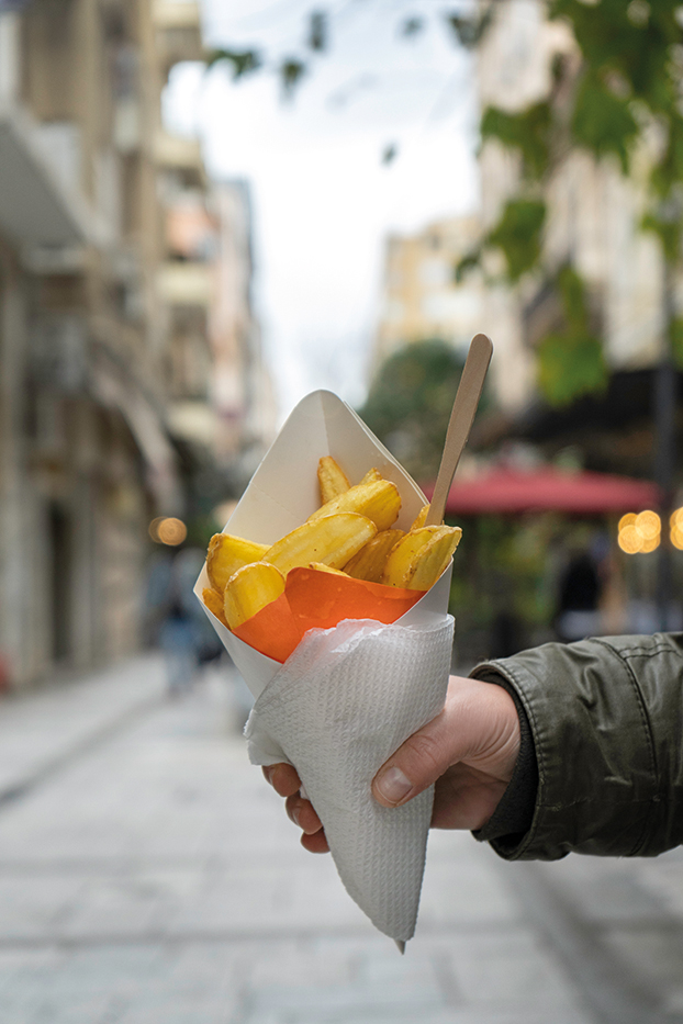 Ένα χάρτινο χωνάκι γεμάτο χρυσαφένιες τραγανές τηγανιτές πατάτες.