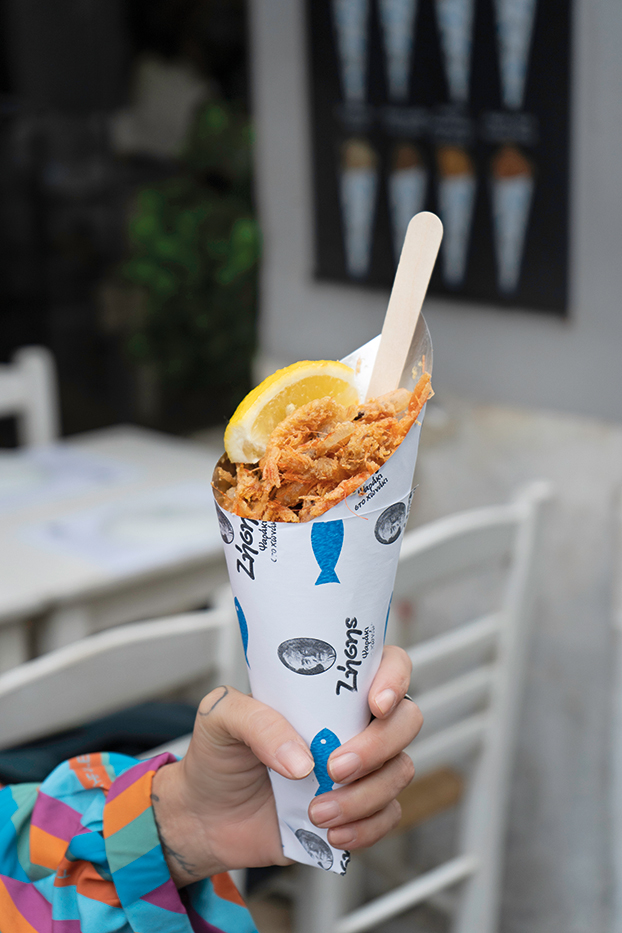 Ένα χέρι κρατάει ένα χάρτινο χωνάκι με τηγανιτές γαρίδες. 