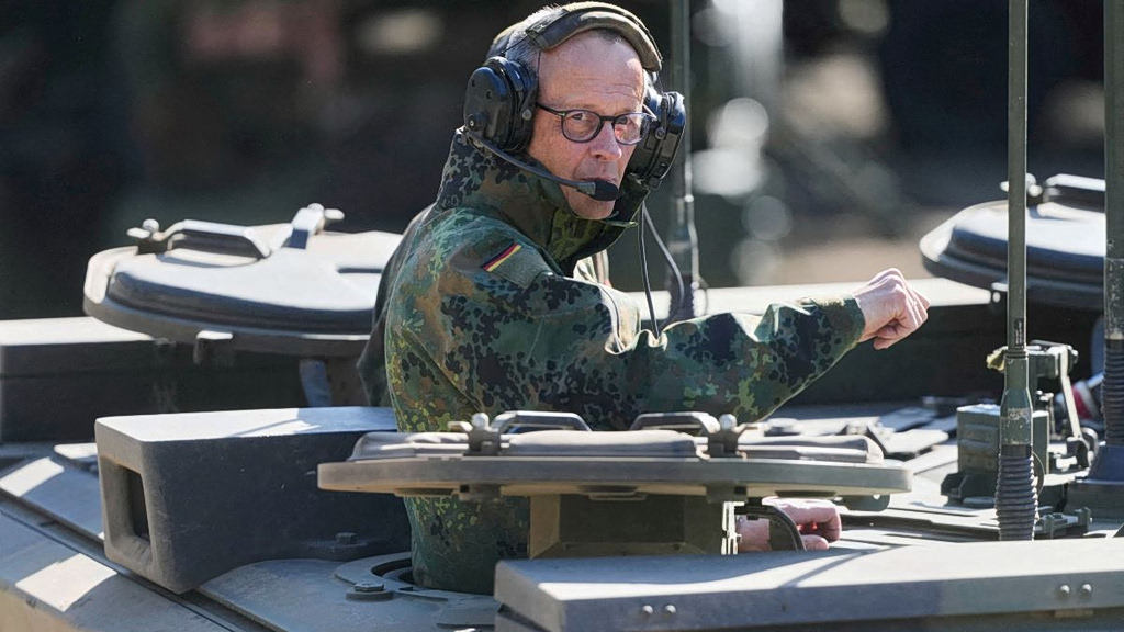 Μερτς: Έστειλε μήνυμα συμφιλίωσης σε Τραμπ πάνω σε άρμα μάχης, με στολή παραλλαγής