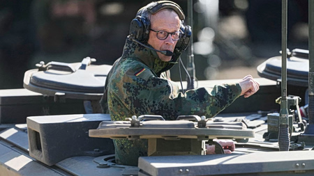 Μερτς: Έστειλε μήνυμα συμφιλίωσης σε Τραμπ πάνω σε άρμα μάχης, με στολή παραλλαγής